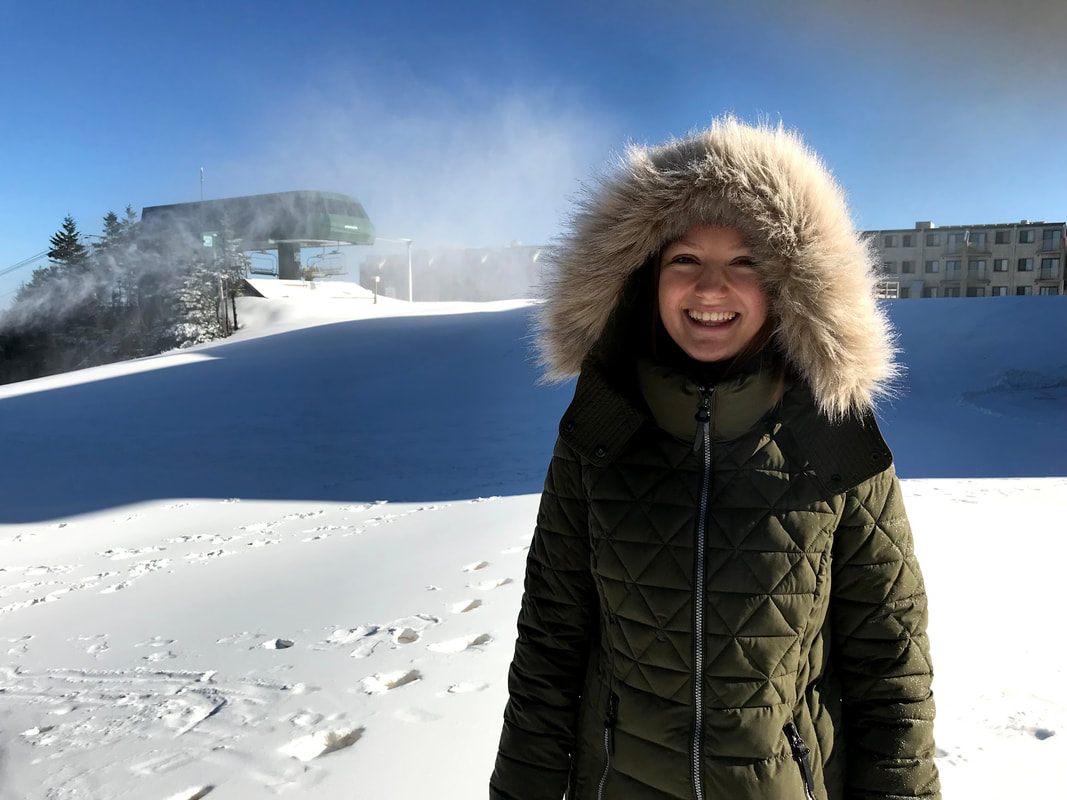 Phoebe grins in front of a snowy hillside, face shrouded by her fuzzy green parka.