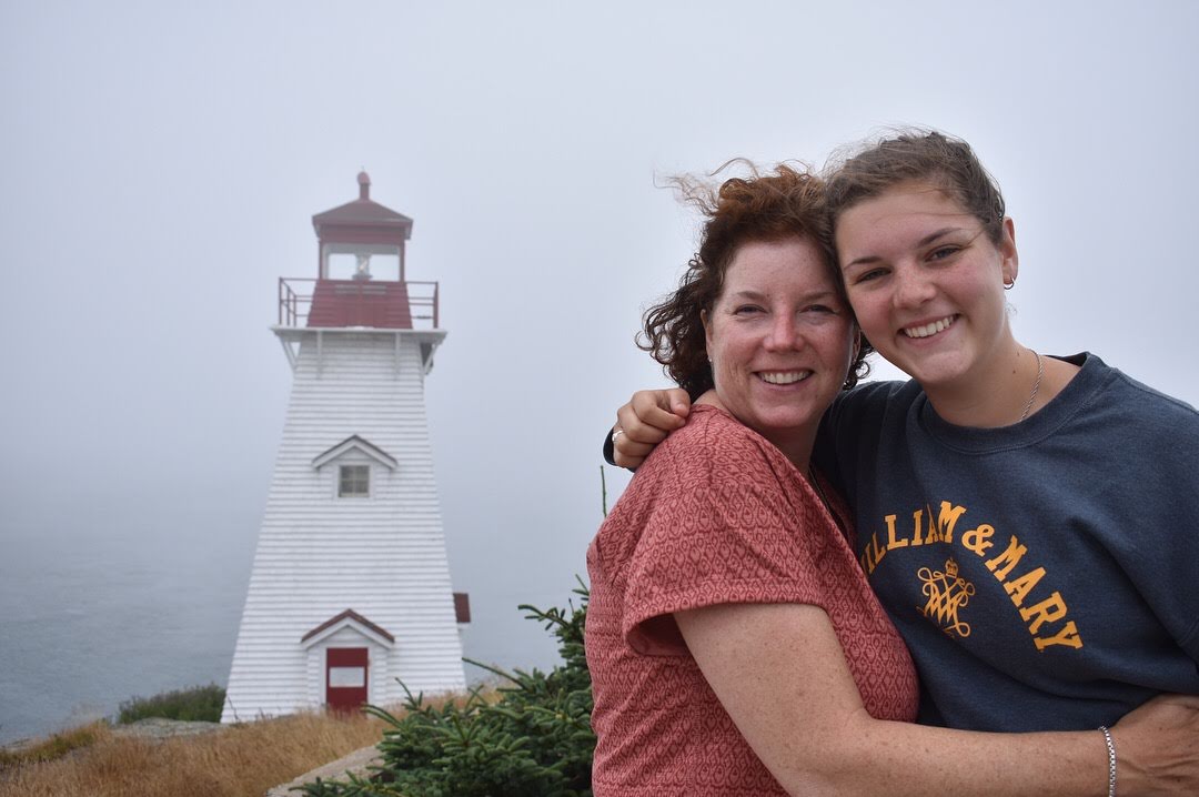 My mother and sister grin, hugging, in front of a lighthouse.